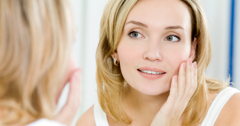 A woman looks in the mirror and ponders facial rejuvenation options.