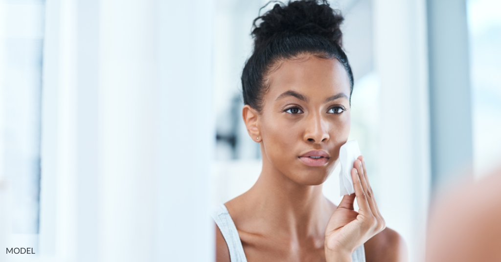 A woman cleansing her skin, looking in the mirror (model)