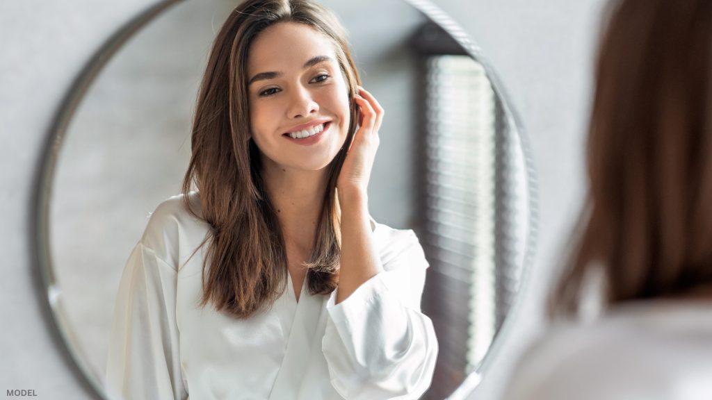 Woman looking in mirror touching face (model)